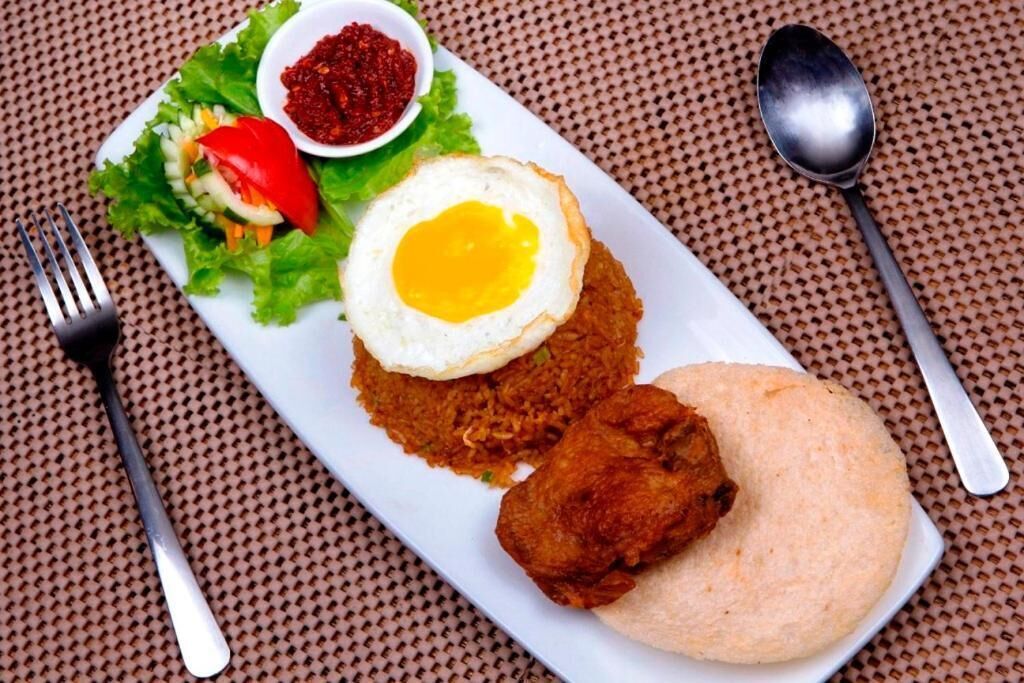 Ein Teller mit gebratenem Reis, einem Spiegelei, einem Stück gebratenem Hähnchen und einem Fladenbrot, dazu ein kleiner Salat und eine Schale Soße.
