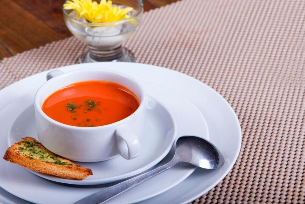 Un bol de soupe blanche, posé sur une assiette blanche, avec une cuillère à côté, et une tranche de pain.