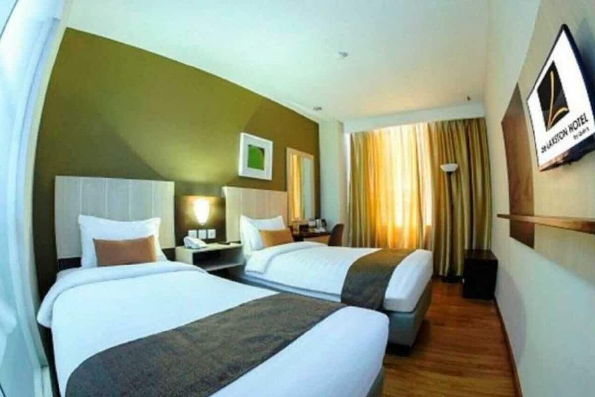 Une chambre d’hôtel avec deux lits, une table de chevet, une lampe et un cadre photo accroché au mur.