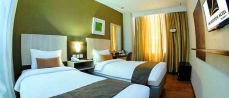 A hotel room with two beds, a nightstand, a lamp, and a picture frame on the wall.
