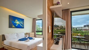 A modern hotel room with a bed, a small desk, a balcony with a table and chairs, and a painting on the wall. - The Lago Apartments by Tropiclook (Rawai)