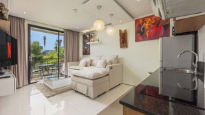 A modern living space with a sofa, a dining area, a kitchen with a built-in oven, and a balcony with a view. - The Lago Apartments by Tropiclook (Rawai)