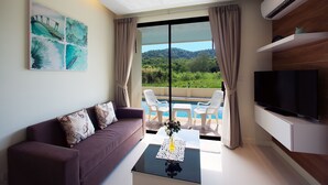 A modern living room with a sofa, a coffee table with a vase, a TV, and a pool view. - The Lago Apartments by Tropiclook (Rawai)