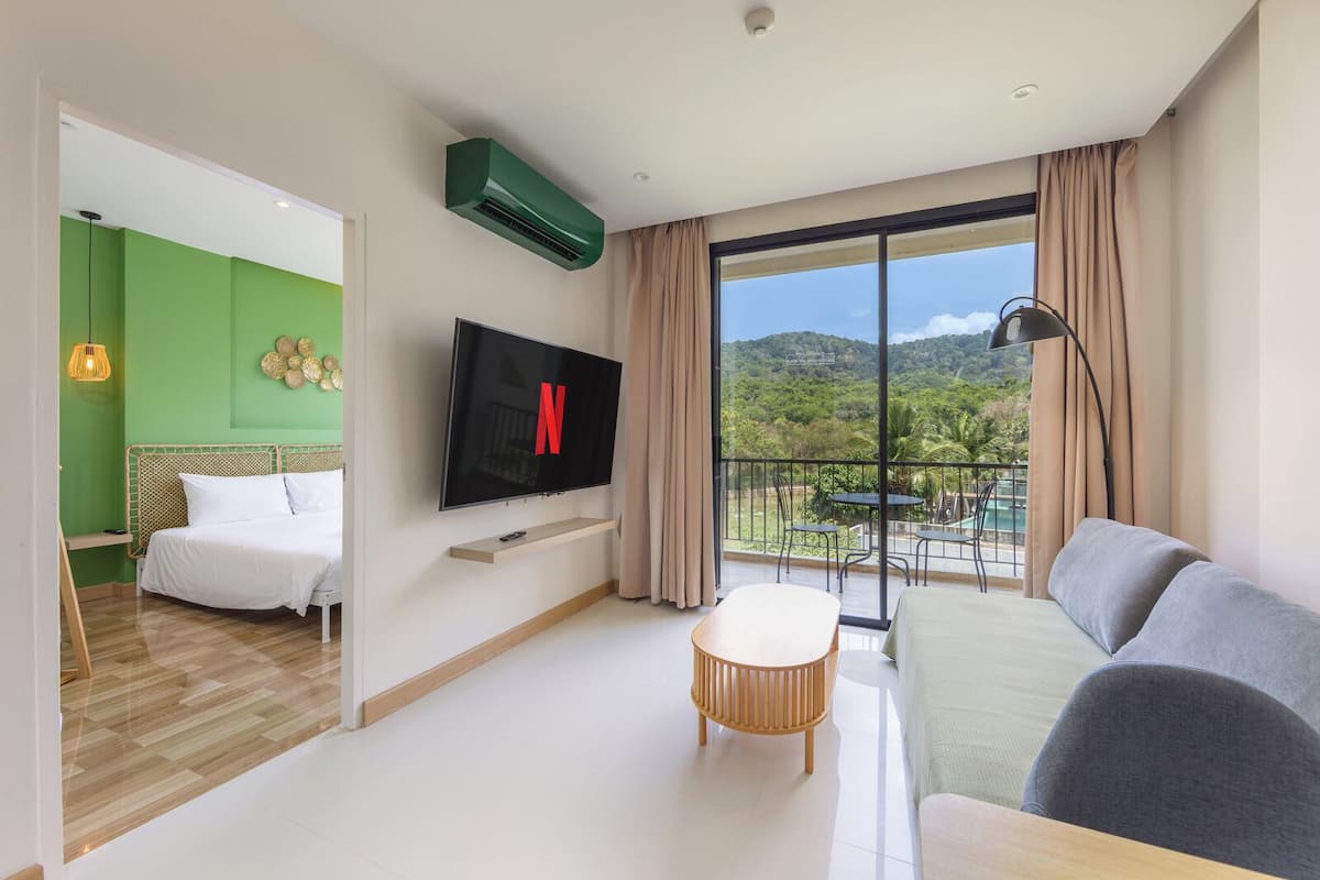 A modern hotel room with a flat-screen TV, a balcony with a pool view, a bed, and a sofa.