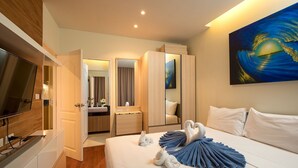 A hotel room with a bed, a TV, a bathroom, and a painting on the wall. - The Lago Apartments by Tropiclook (Rawai)