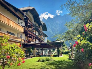 A traditional chalet with a balcony, a garden with flowers, and a mountain backdrop. - Post Hotel Mittenwald (Mittenwald)