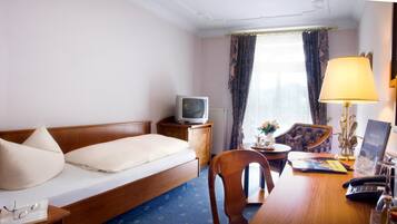 A hotel room with a bed, a desk with a lamp, a chair, a television, and a window with curtains.