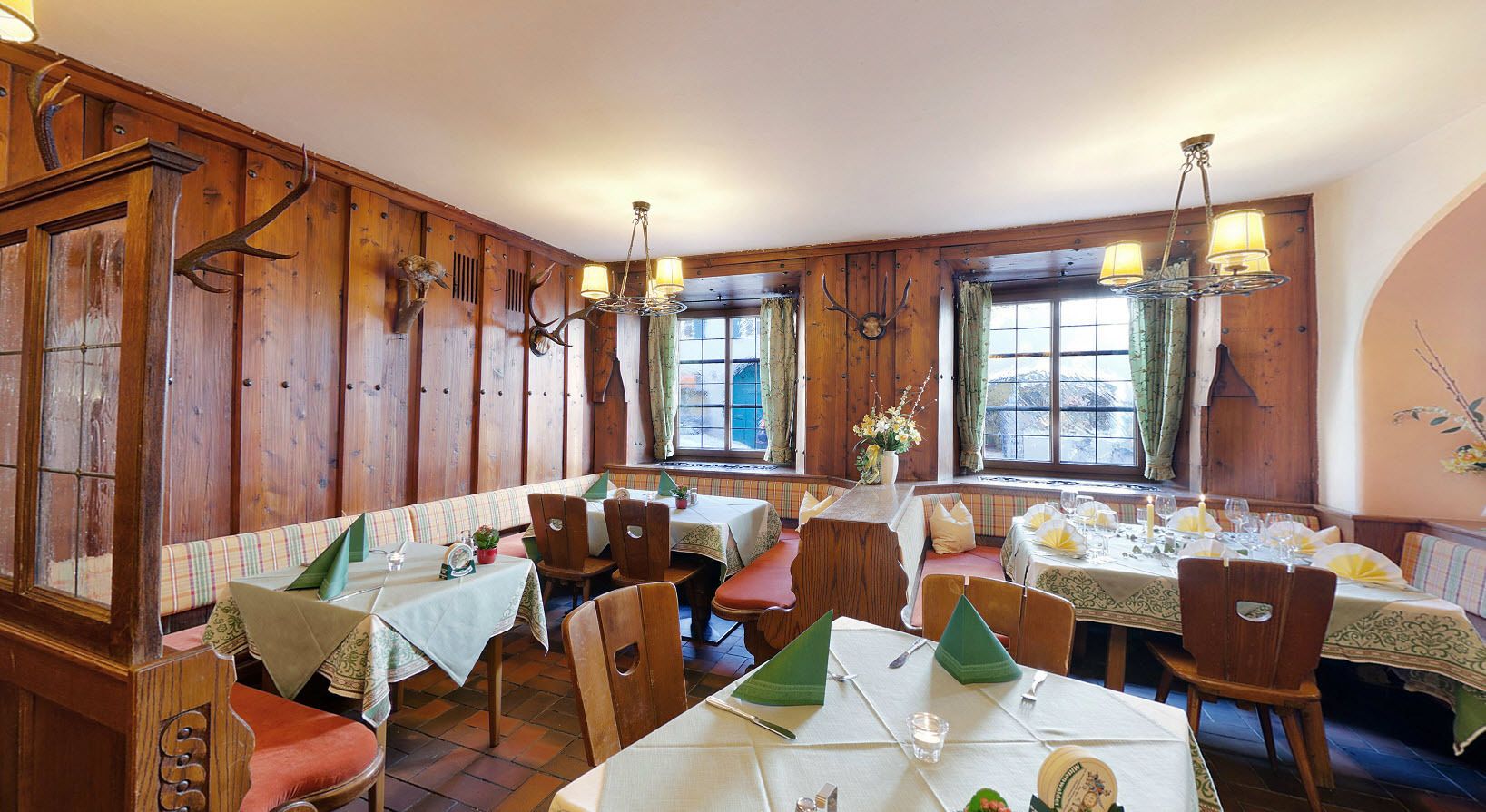 A restaurant with wooden paneled walls, multiple tables with green tablecloths, and a cozy ambiance.