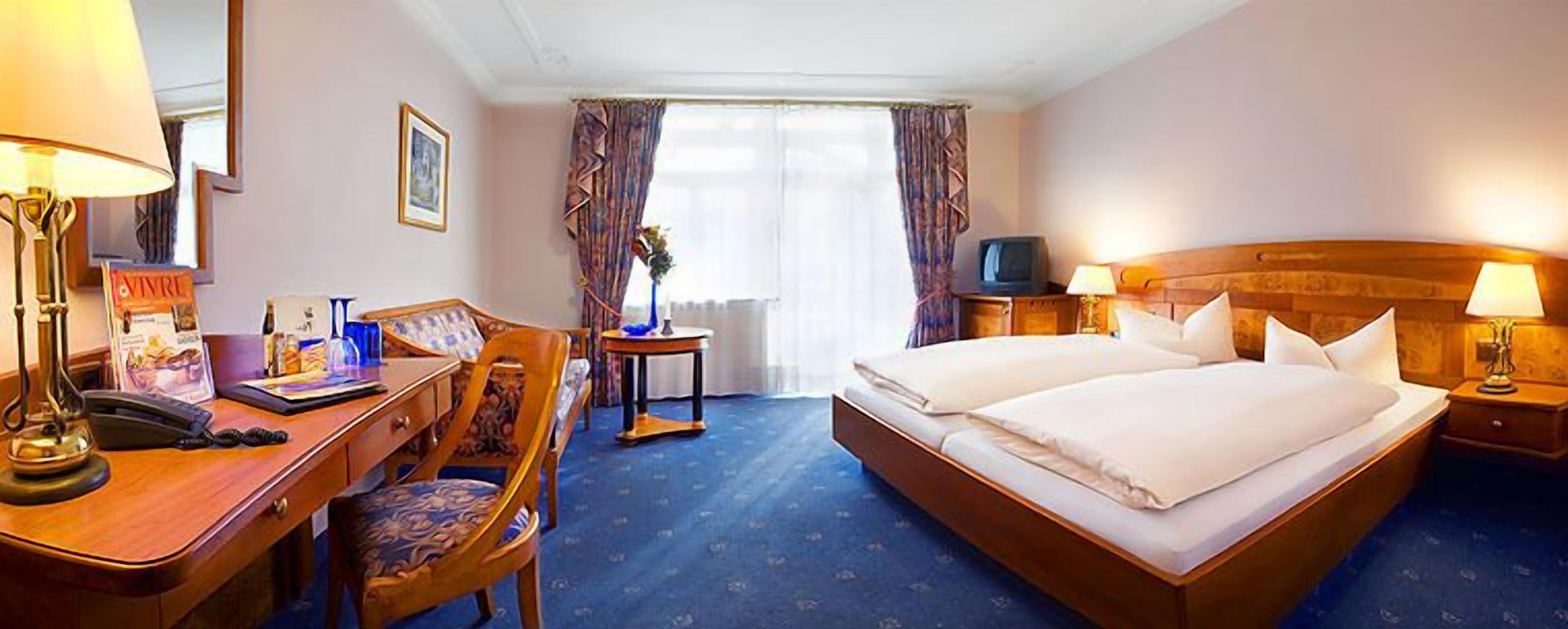 A hotel room with a desk, two beds, a television, and a window with curtains.