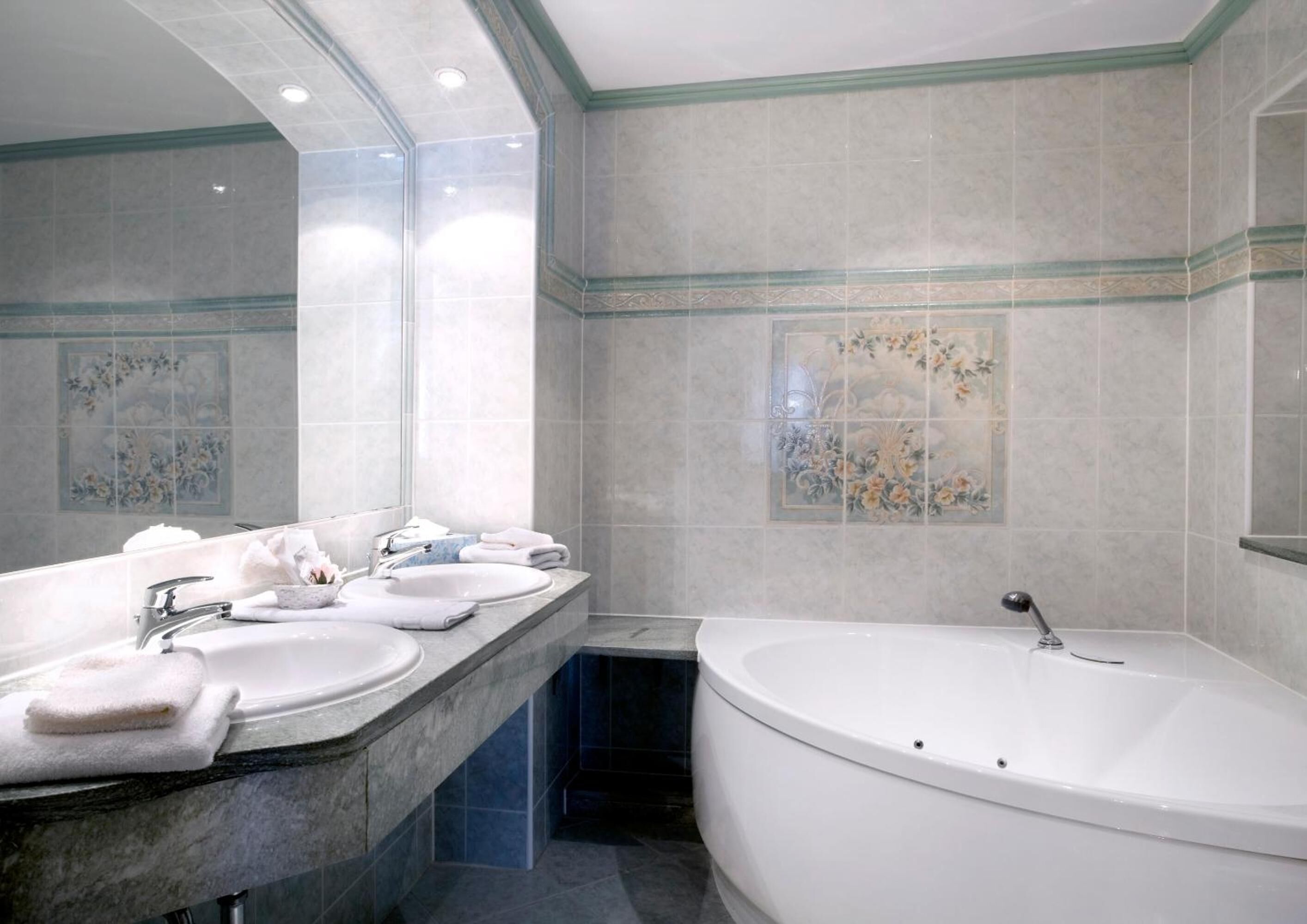 A bathroom with a large bathtub, a vanity with three sinks, and decorative tiles.