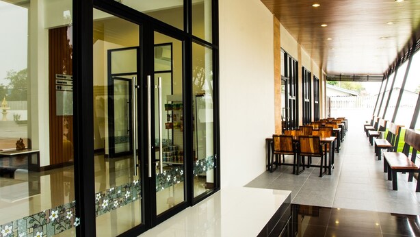 A hotel lobby with a long corridor, large windows, and a seating area with wooden chairs and tables. - NP Hotel (Buriram)
