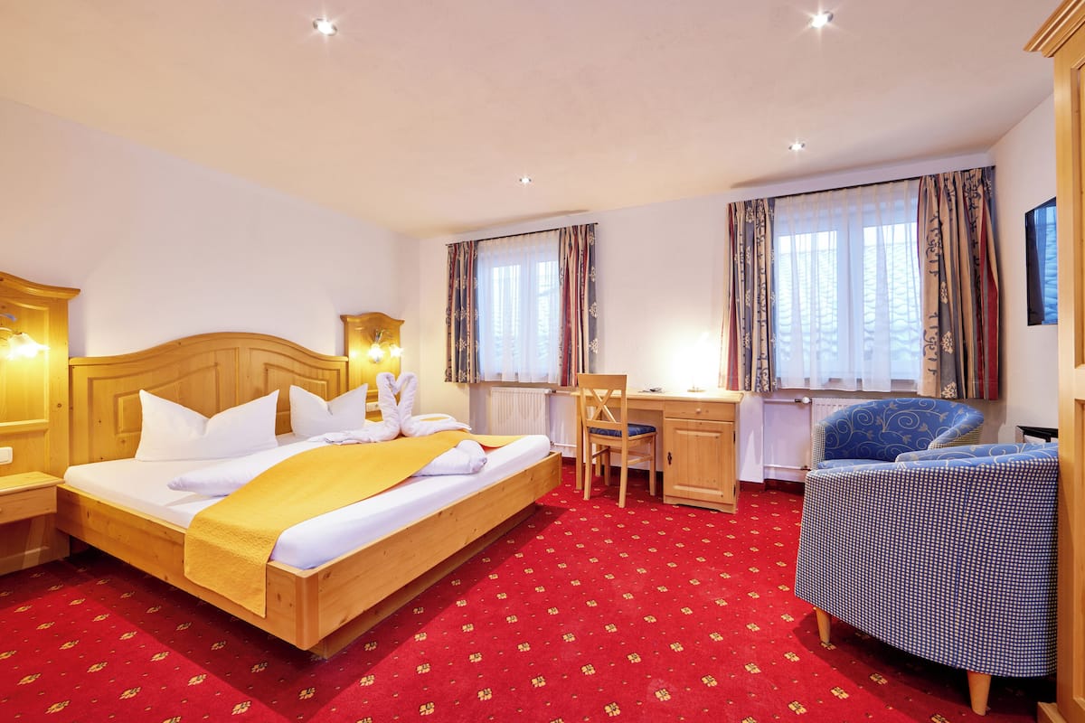 A hotel room with a wooden bed, a desk, a chair, and a red carpet.