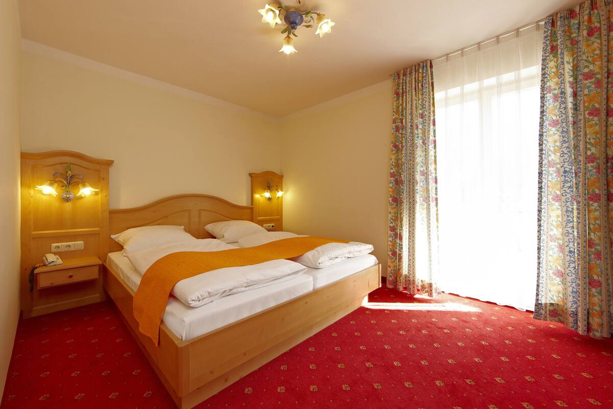 A hotel room with a wooden bed, two bedside tables with lamps, a red carpet, and floral curtains.