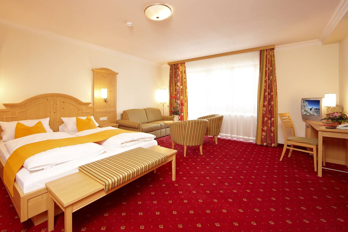 A hotel room with a large bed, a wooden nightstand, a desk with a computer, a chair, and a sofa.