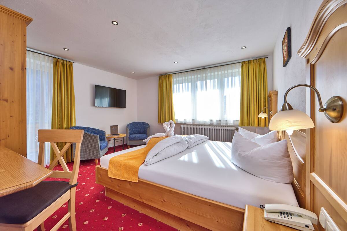 A hotel room with a bed, wooden furniture, a desk, a chair, a TV, and a window with curtains.