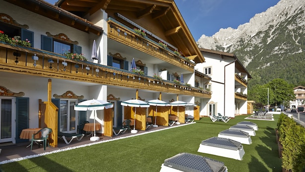 A hotel with outdoor seating, a well-maintained lawn, and a mountain backdrop. - Alpenhotel Rieger (Mittenwald)