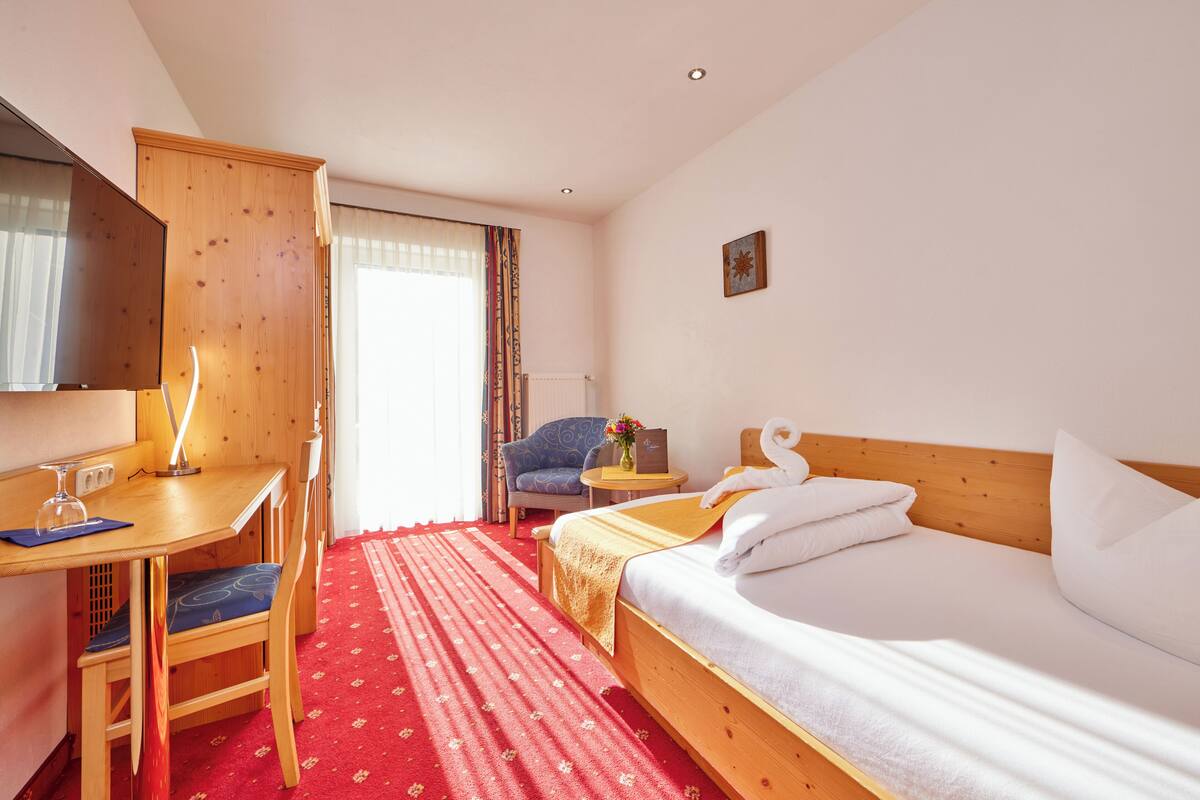 A hotel room with a wooden bed, a desk with a chair, a television, and a window with curtains.