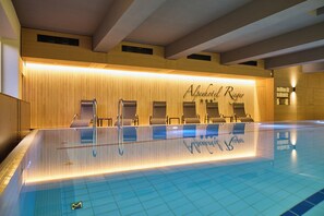 A swimming pool area with a reception desk, lounge chairs, and a tiled floor.