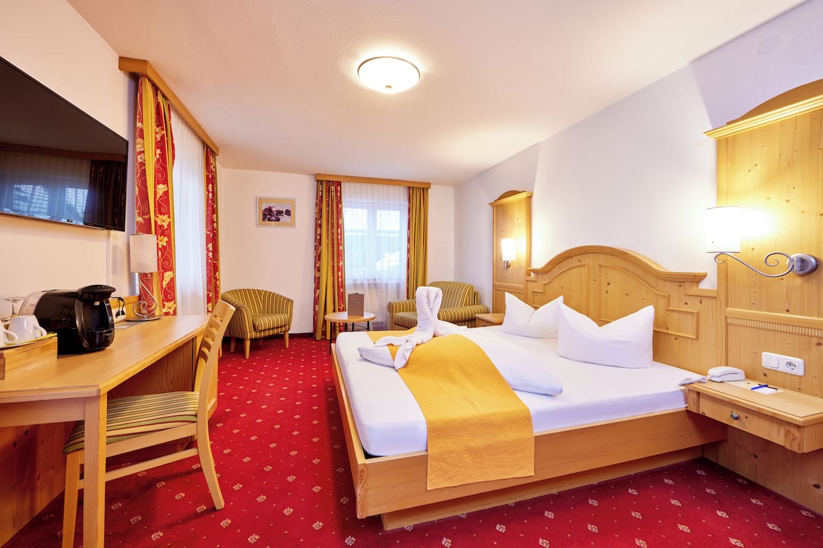 A hotel room with a bed, a desk, a chair, a small table, and a mirror.