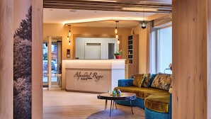A modern hotel lobby with a reception desk, a blue sofa, and a small table with decorative items. - Alpenhotel Rieger (Mittenwald)