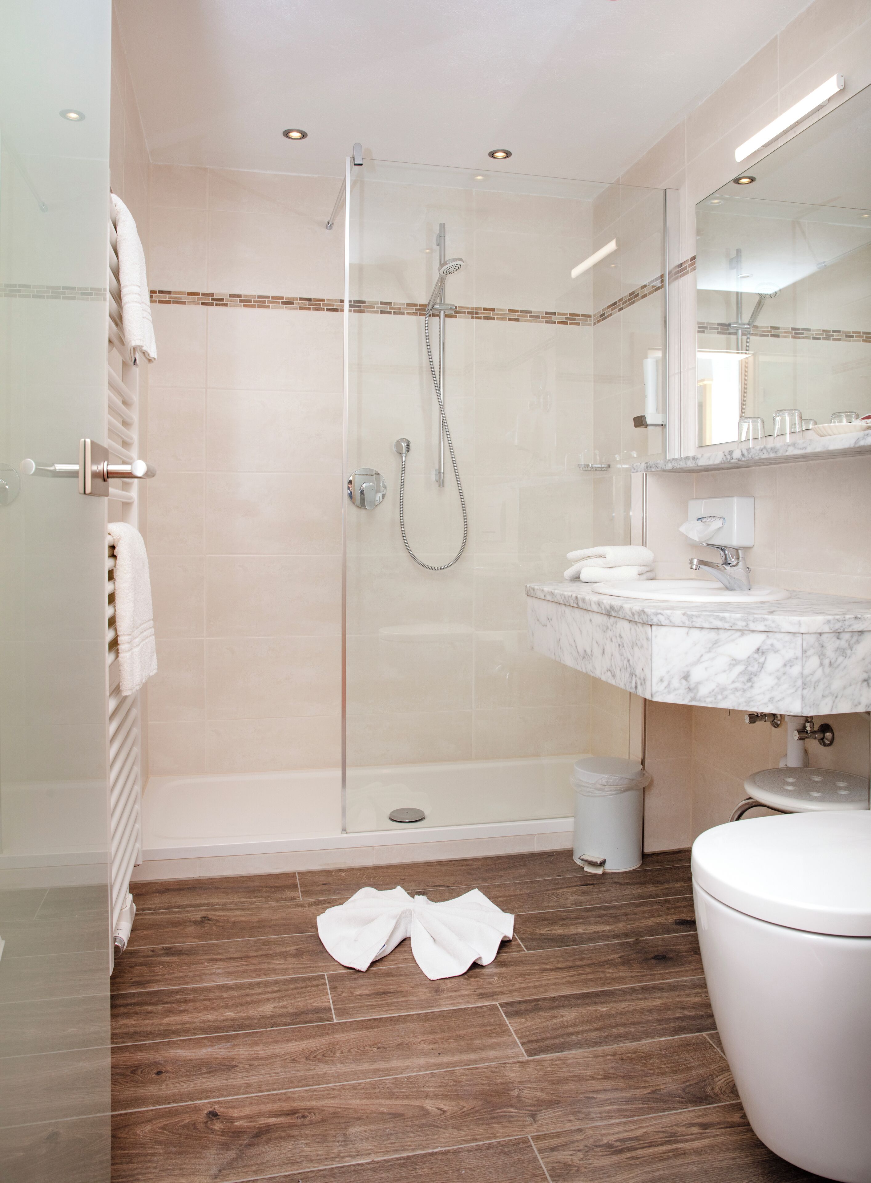 Ein modernes Badezimmer mit einer gläsernen Duschkabine, einem мраморному Waschbecken und Holzboden.