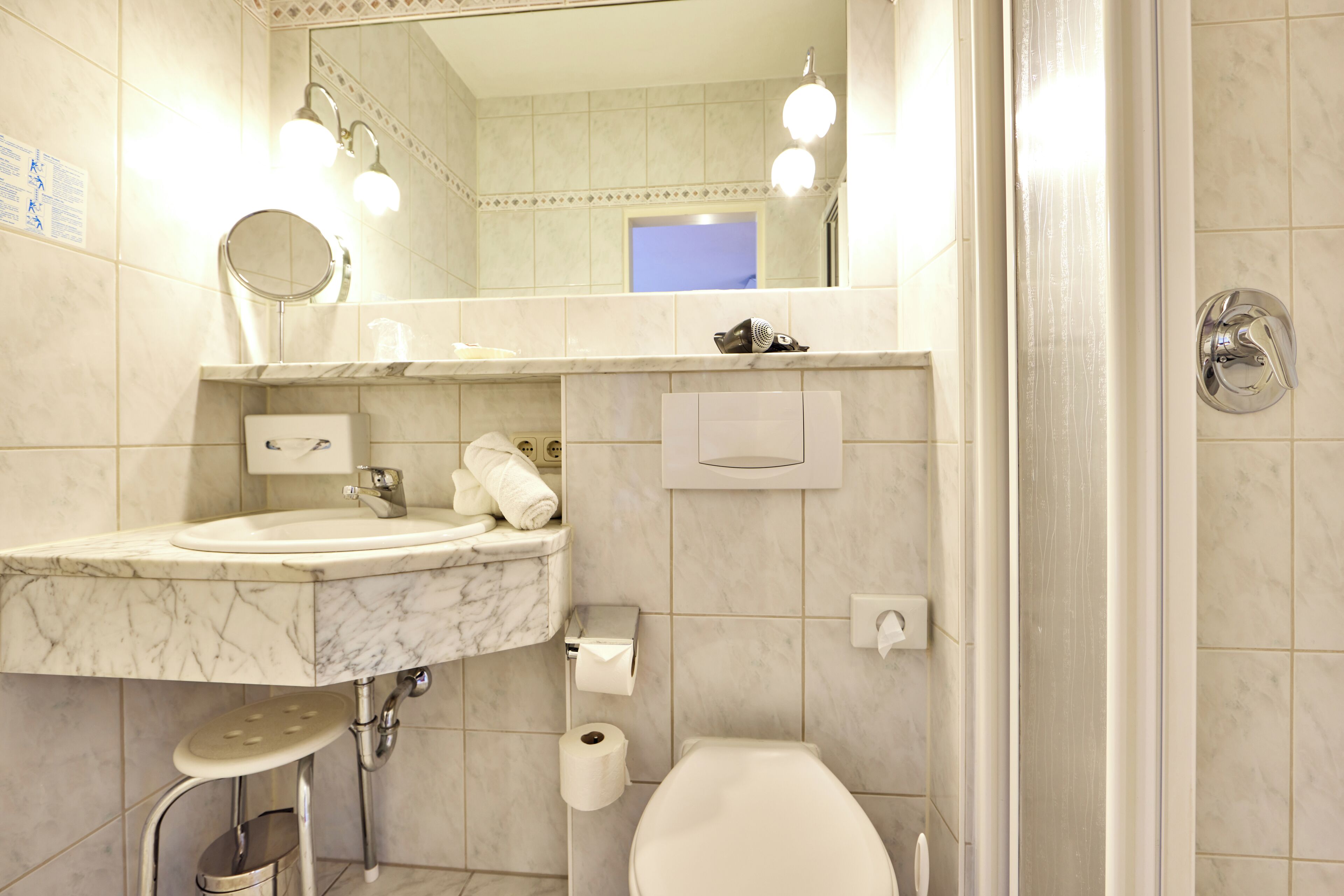 Une salle de bain avec un lavabo en marbre, des toilettes, un miroir et un espace douche.