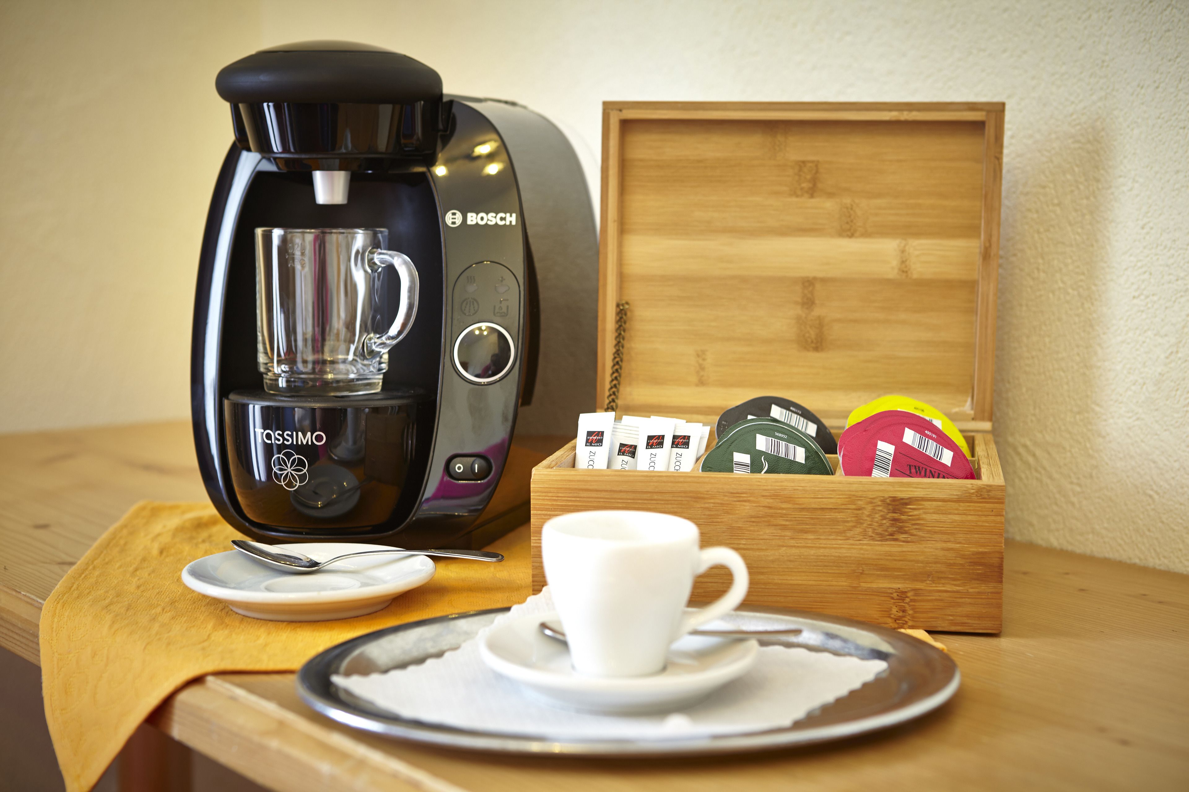 A coffee maker, a cup, and a box of coffee pods on a wooden table.