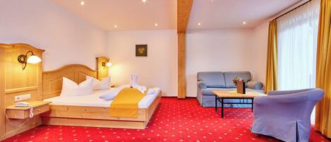 A hotel room with a wooden bed, a sofa, a chair, a small table, and a red carpet.