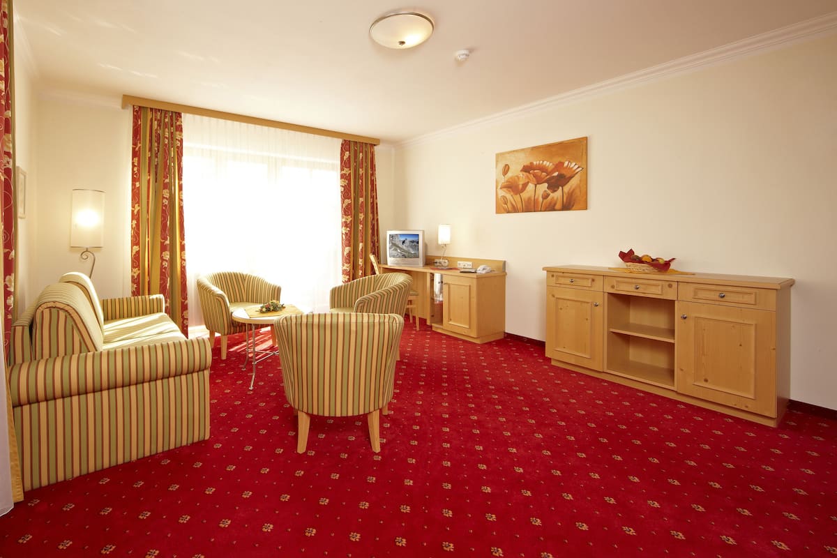 A hotel room with striped armchairs, a small dining table, a TV, and a wooden cabinet.