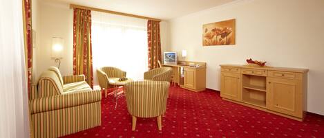 Una habitación de hotel con sillones a rayas, una pequeña mesa de comedor, un televisor y un armario de madera.