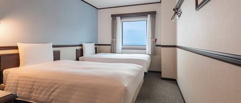 A hotel room with two beds, a window with curtains, a headboard, and a wall-mounted light fixture.