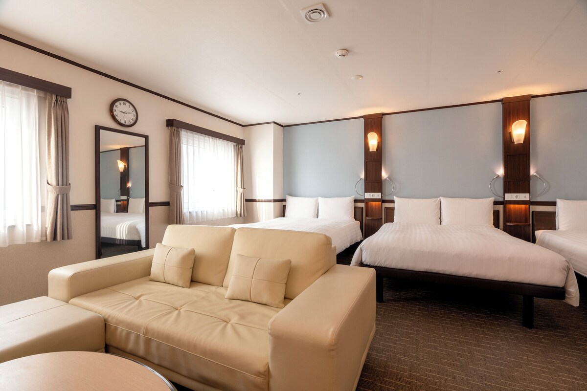 Et hotelværelse med en sofa, to senge, et spejl og et ur på væggen.