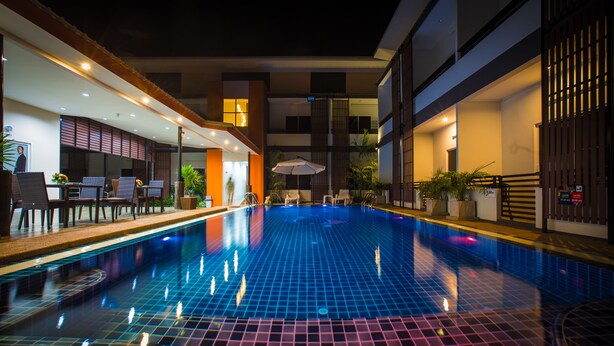 A swimming pool with tiled flooring, surrounded by lounge chairs and tables, and adjacent to a building with a modern design. - The S.G Hotel (Buriram)