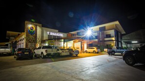 A hotel with a modern facade, a parking lot with several cars, and a brightly lit entrance. - The S.G Hotel (Buriram)