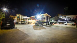 A parking lot with multiple vehicles, including SUVs and a van, in front of a building with a sign that reads "TRESOR HOTEL". - The S.G Hotel (Buriram)