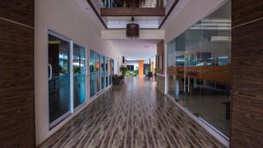 A modern hotel corridor with glass walls, wooden flooring, and a central seating area. - The S.G Hotel (Buriram)