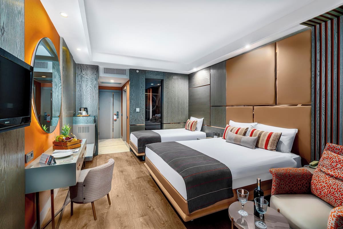 Ett modernt hotellrum med två sängar, ett skrivbord, en stol, en TV och en minibar.