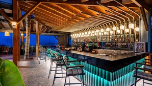 A bar area with a long counter, multiple bar stools, and a ceiling with exposed wooden beams and hanging lights. - Arycanda Kirman Premium - Ultra All Inclusive (Alanya)