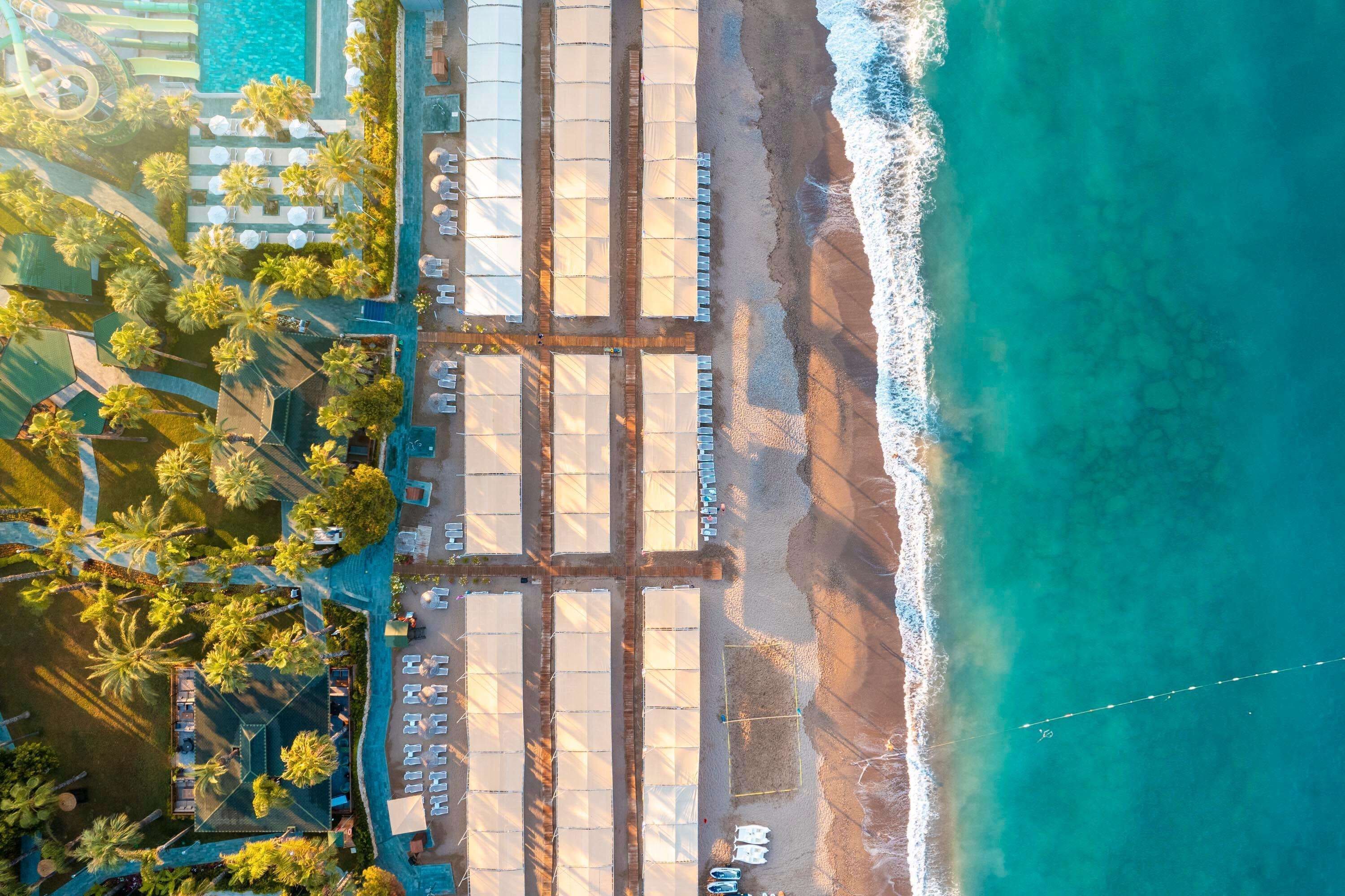 Vista aérea de un resort con zona de playa, palmeras y una piscina.