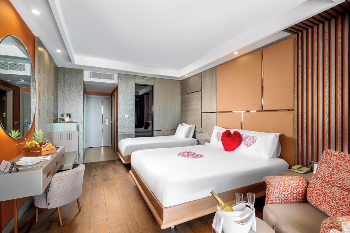 Ett hotellrum med två sängar, ett skrivbord, en stol, en minibar och en stor spegel.