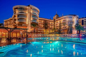 A hotel with a large swimming pool, multiple balconies, and a covered outdoor area with seating. - Arycanda Kirman Premium - Ultra All Inclusive (Alanya)