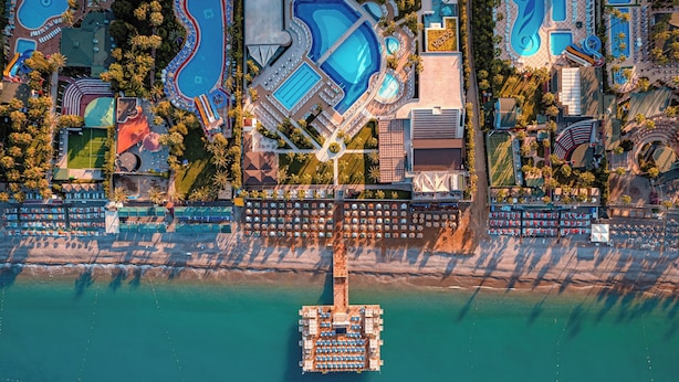 Vue aérienne d’un complexe hôtelier doté de plusieurs piscines, d’une plage et d’un quai.