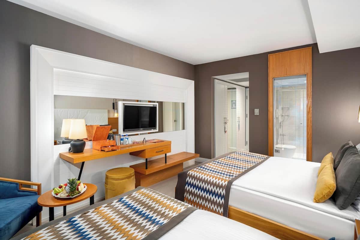 Une chambre d’hôtel avec un lit, un bureau équipé d’un ordinateur, une télévision et une salle de bain visible à travers une porte en verre.