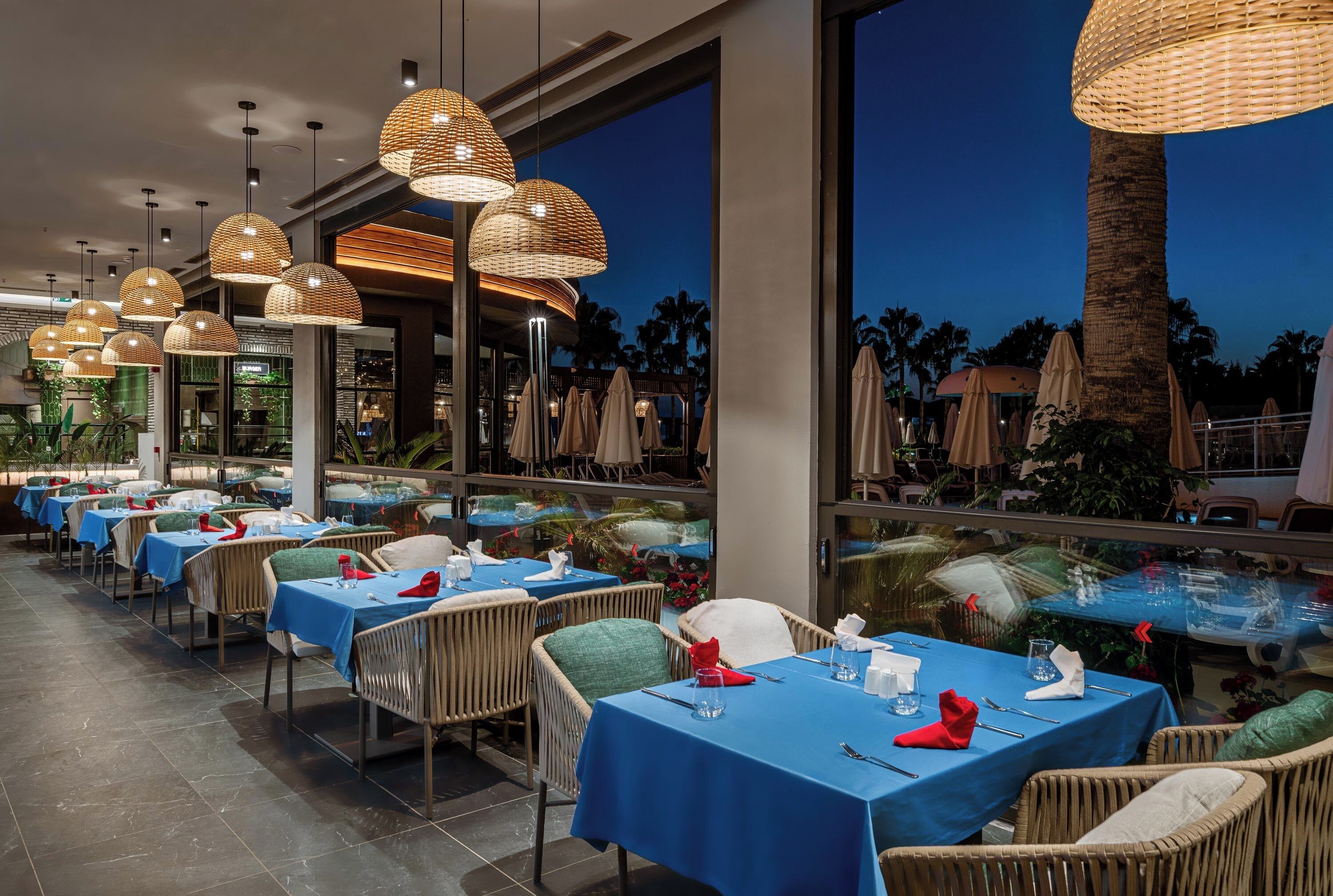 A restaurant with tables set for dining, wicker chairs, and hanging pendant lights.