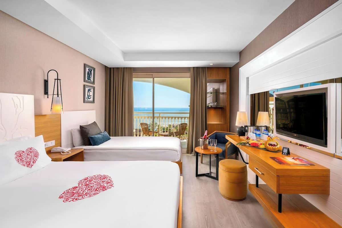 Une chambre d’hôtel avec deux lits, un bureau avec une télévision et un balcon avec vue.