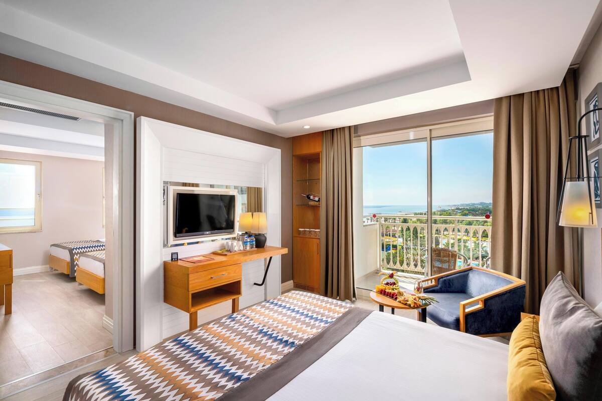 Une chambre d’hôtel avec un lit, un bureau avec une télévision, un balcon avec vue et une chaise.