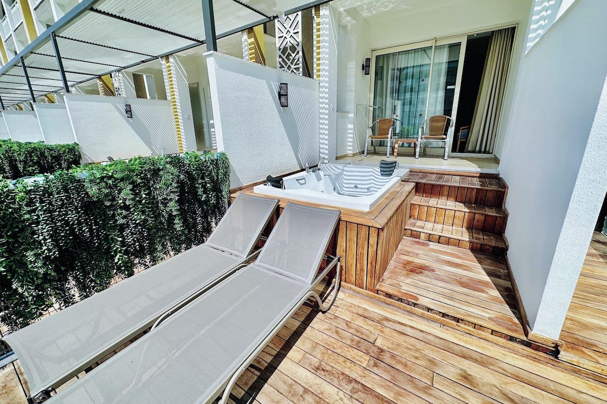 Un espace extérieur ensoleillé avec une terrasse en bois, un jacuzzi et des chaises longues.