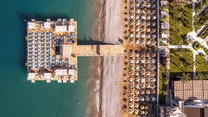 Vue aérienne d’un complexe hôtelier situé en bord de mer, avec une zone d’amarrage pour les bateaux, des chaises longues et une terrasse où l’on peut prendre ses repas.