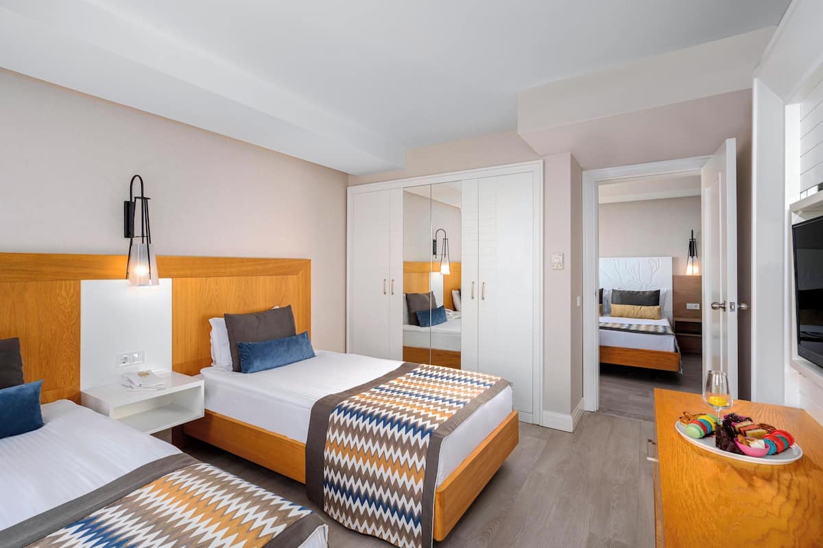 Une chambre d’hôtel avec deux lits, une tête de lit en bois, des tables de chevet, un miroir, une télévision et un plateau de petit-déjeuner.