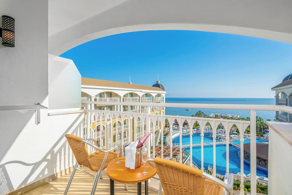 Un balcon avec des fauteuils et une table en osier, donnant sur une piscine et les bâtiments du complexe hôtelier.